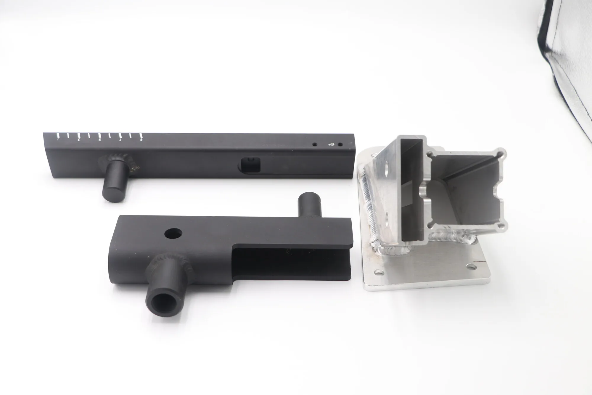 Welded and machined aluminum arm with laser-marked scale alongside a welded bracket assembly